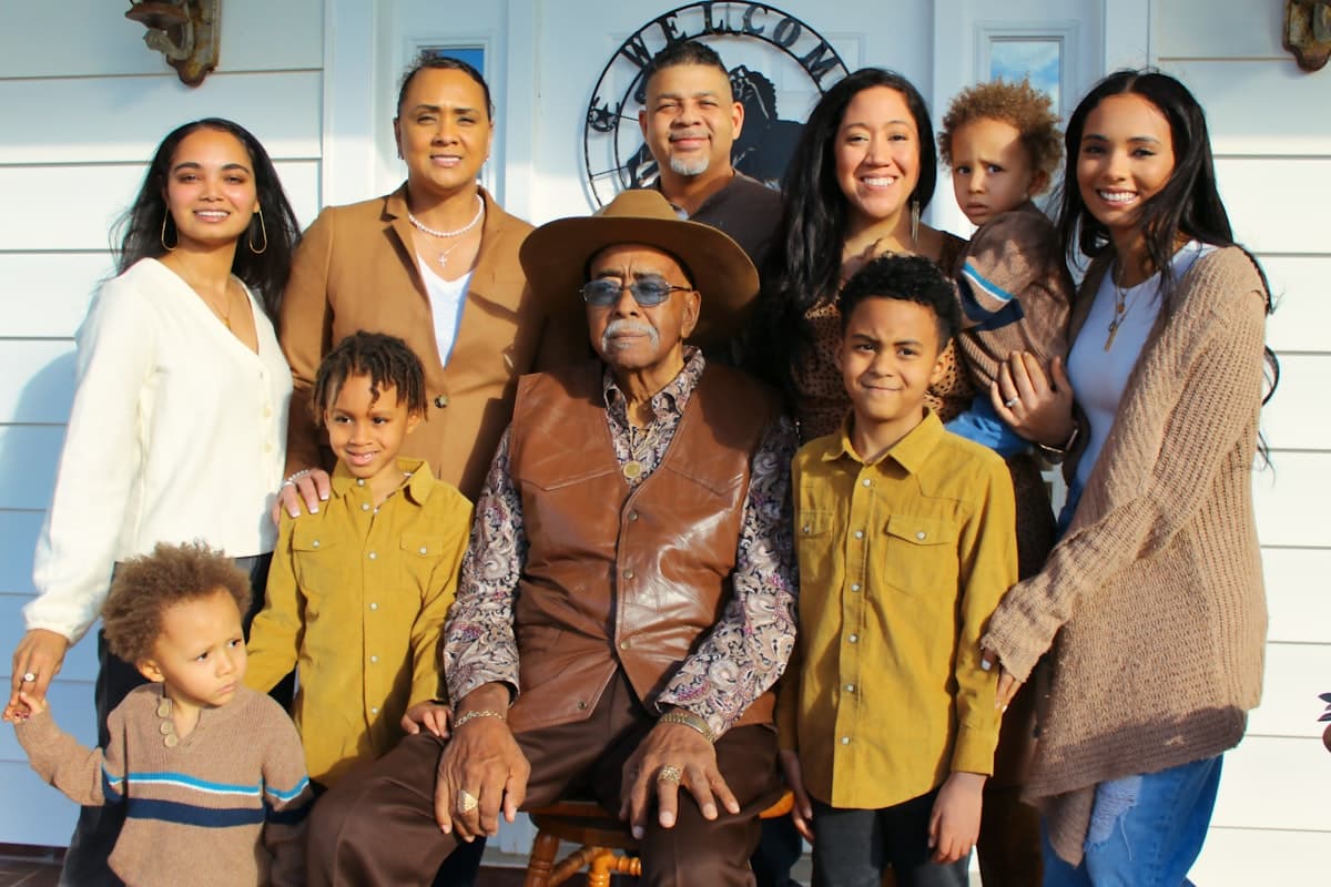 A diverse multigenerational family gathered closely together outdoors, smiling.